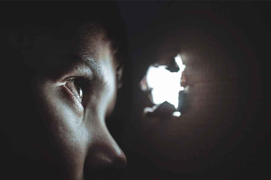 image of woman looking through hole in screen representing the trap of alcohol and drug addiction for Gulf Breeze Recovery landing page –addiction trap