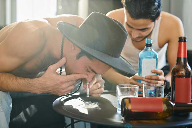 image of young men drinking and snorting lines of illegal drug likely cocaine or heroin. This fr article about news report suggesting that illegal drug use and spending has increased