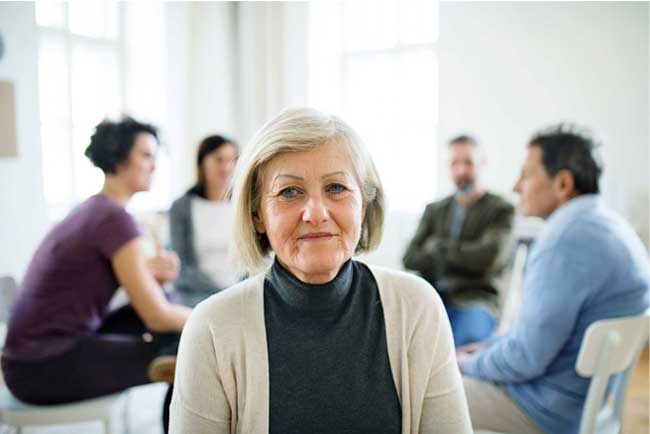 image of woman facing camera with group counseling meeting in the background