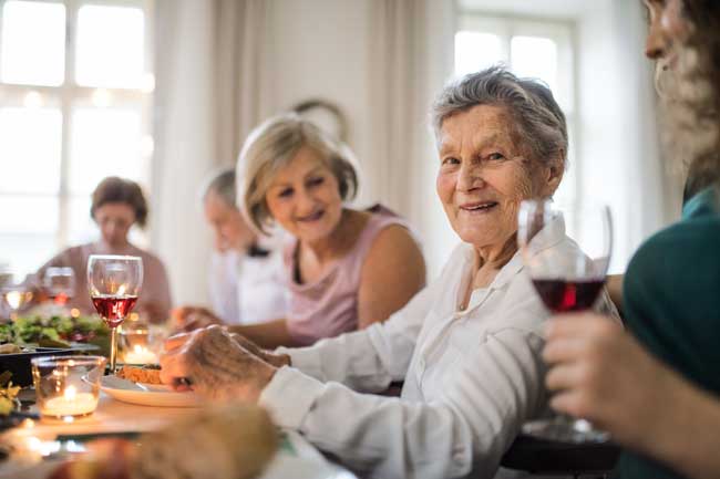 elderly woman facing camera with family drinking wine