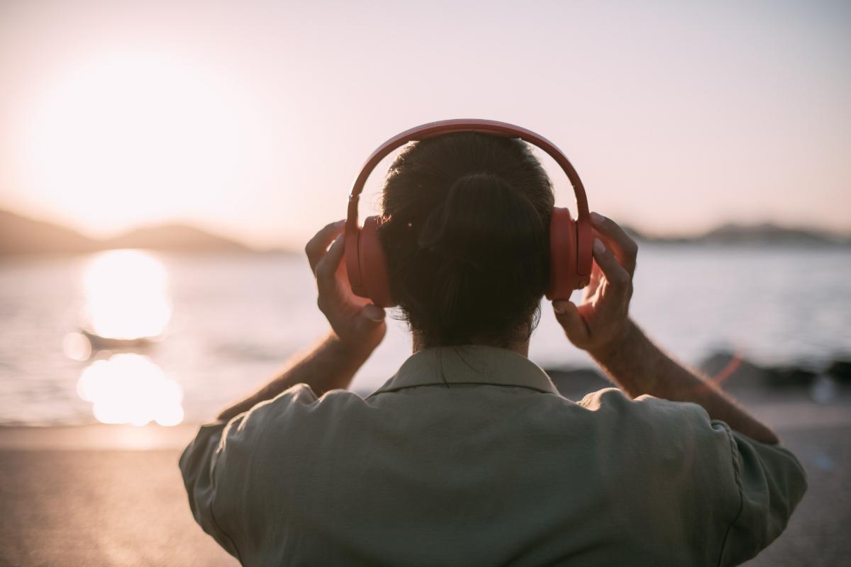 Man listening to music on headphones while watching sunset on the beach reaping the benefits of music and recovery