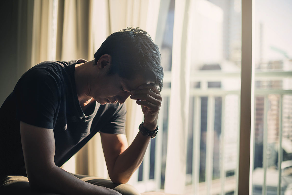 person sitting in dark room hanging head near window while struggling with long-term effects of meth use