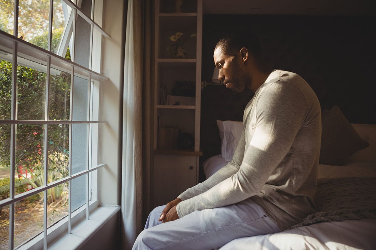 man kneeling by his window suffering from post-acute withdrawal syndrome