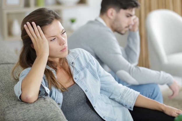 a couple sitting on couch but turned away from each other in anger after discussing addiction and relationships