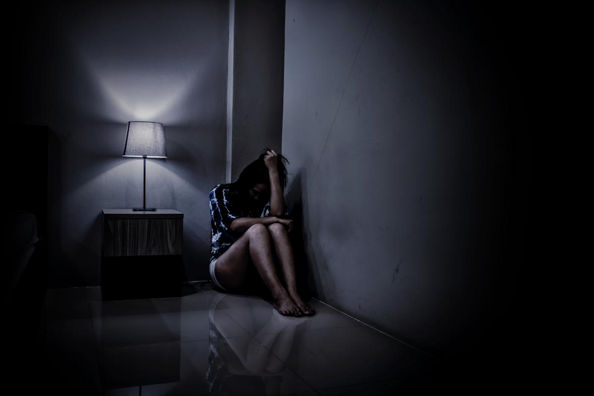 Woman sitting in the corning of a dark room late at night hanging her head while struggling with signs of heroin abuse