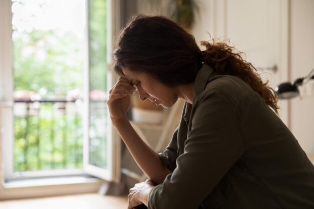 Woman sitting in the dark near a window hanging her head and struggling with substance use during pregnancy