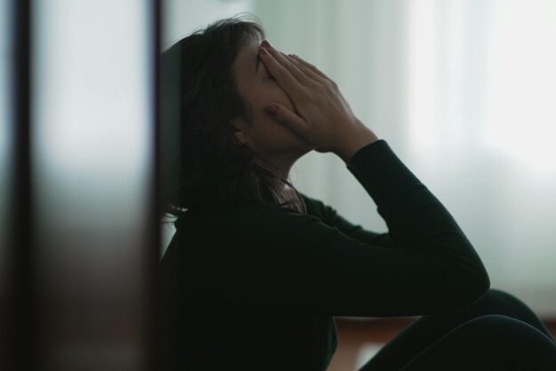 person sitting against wall in dark room with hands over face while struggling with meth symptoms