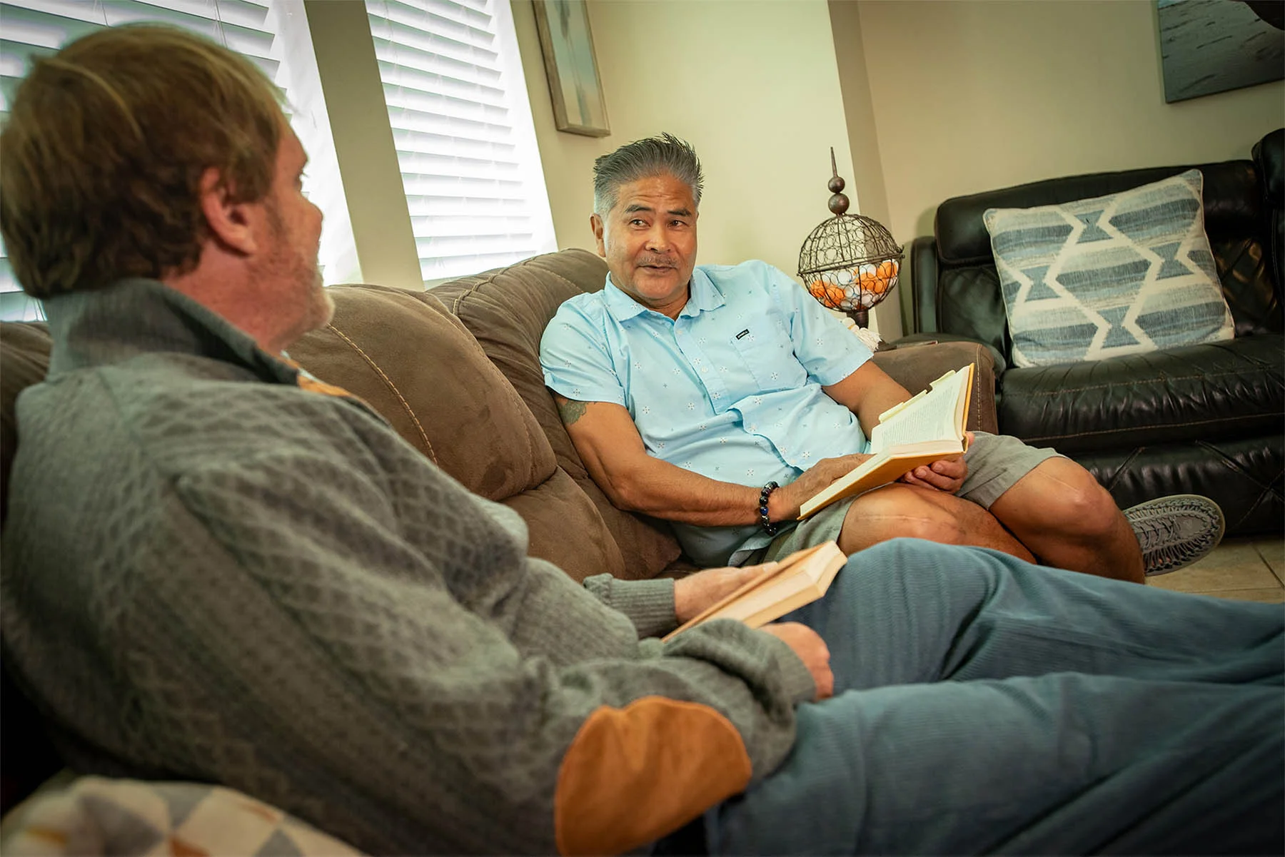 Two men sitting on couch together holding a book.