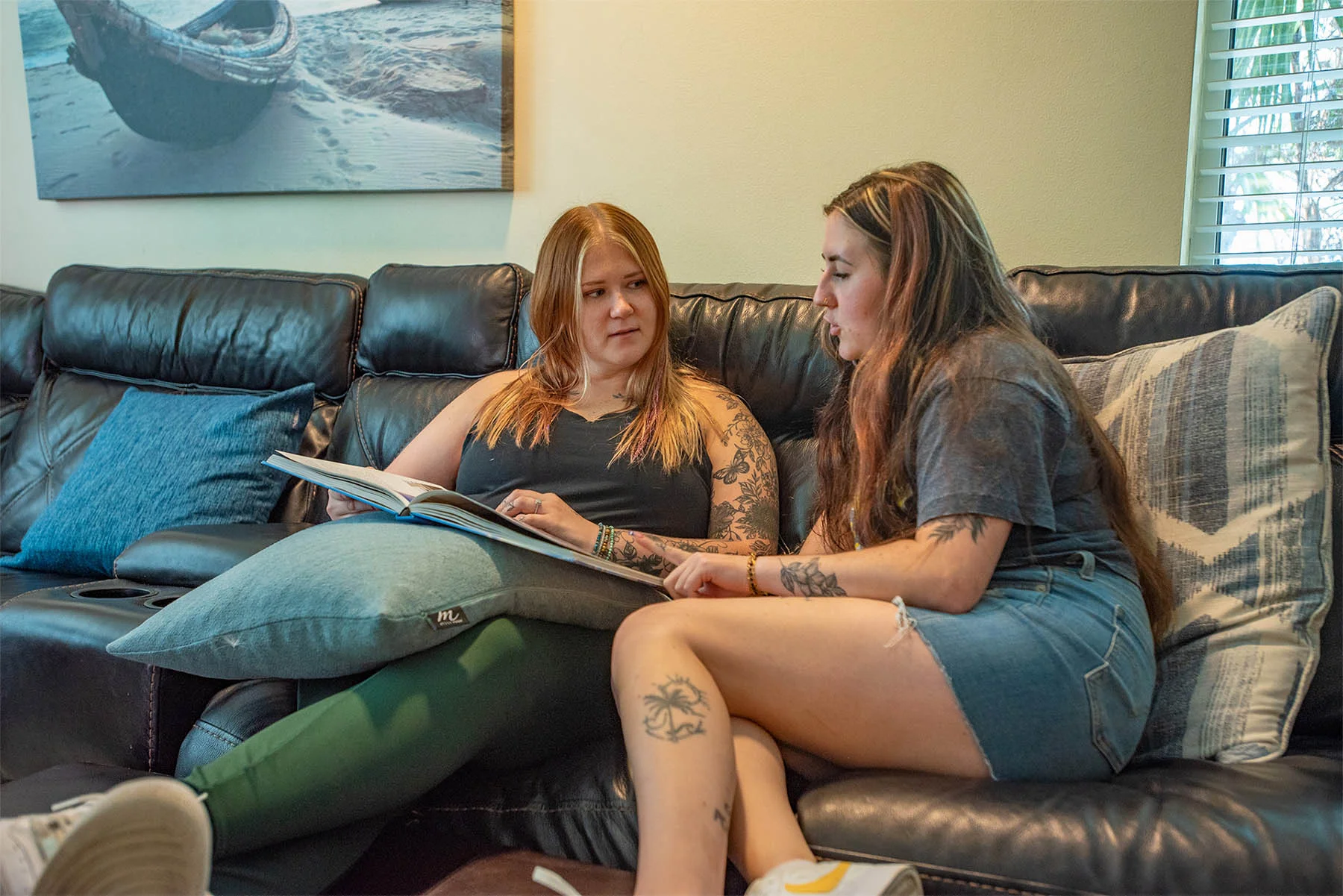 Two women looking at book together on a couch