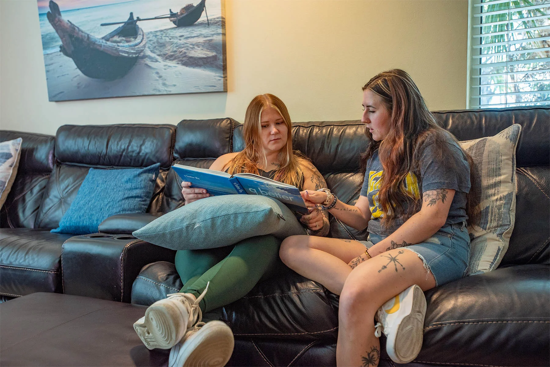 Two women looking at book while sitting on a couch