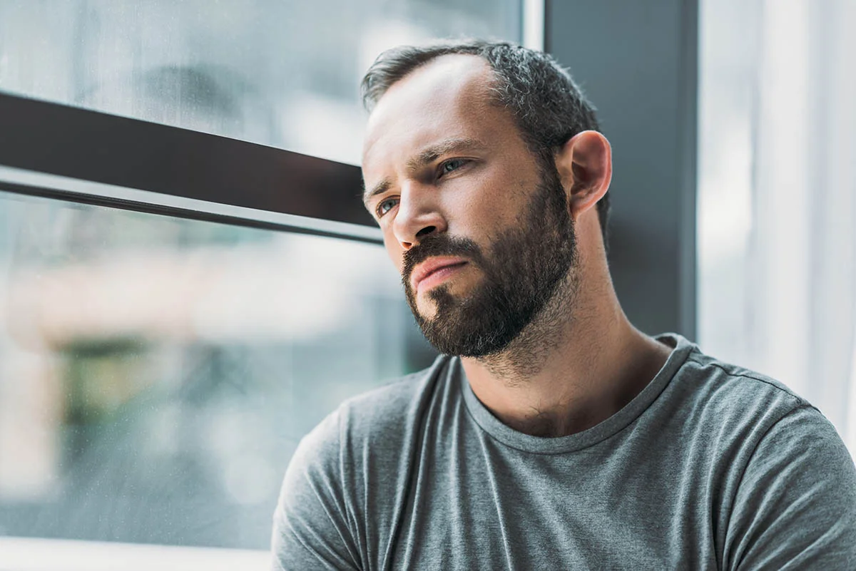Man near window pondering the signs of opioid addiction