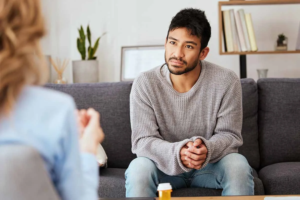 young man sitting on couch talking to therapist who is explaining the challenges of recognizing painkiller addiction