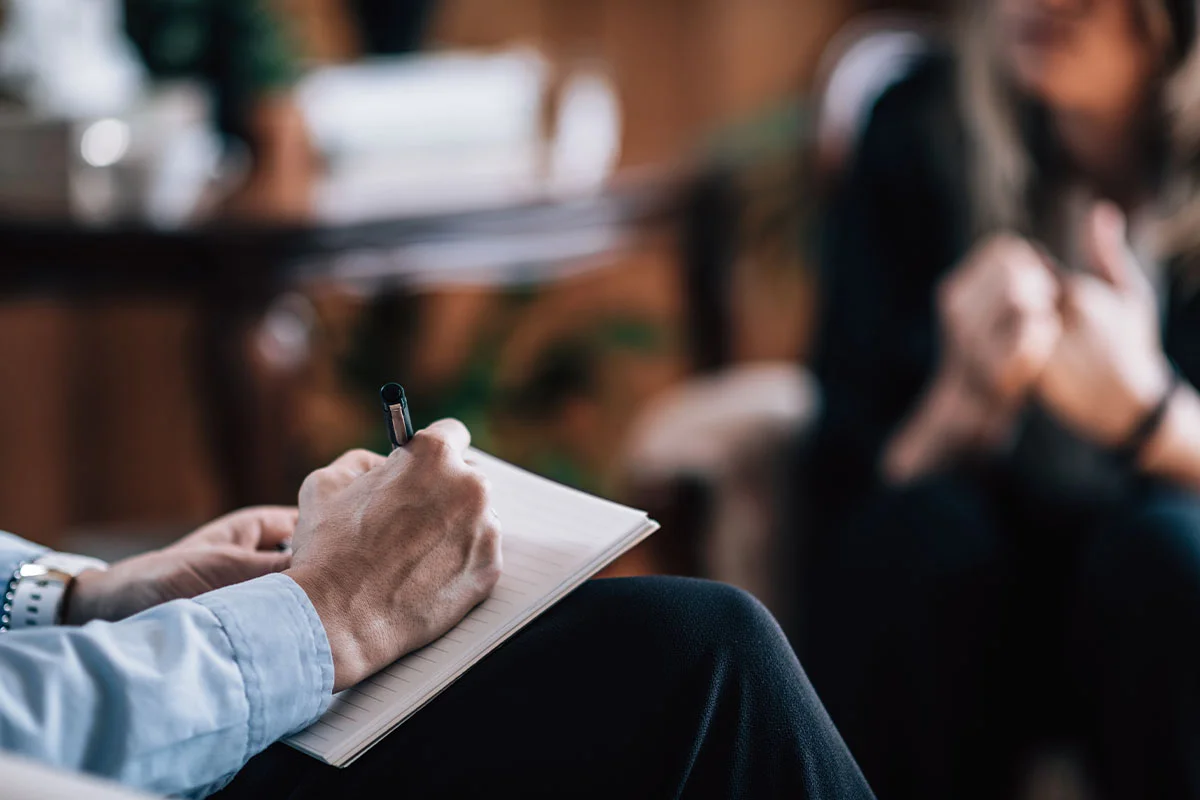 Hands of a mental health professional taking notes as they and their patient ponder
